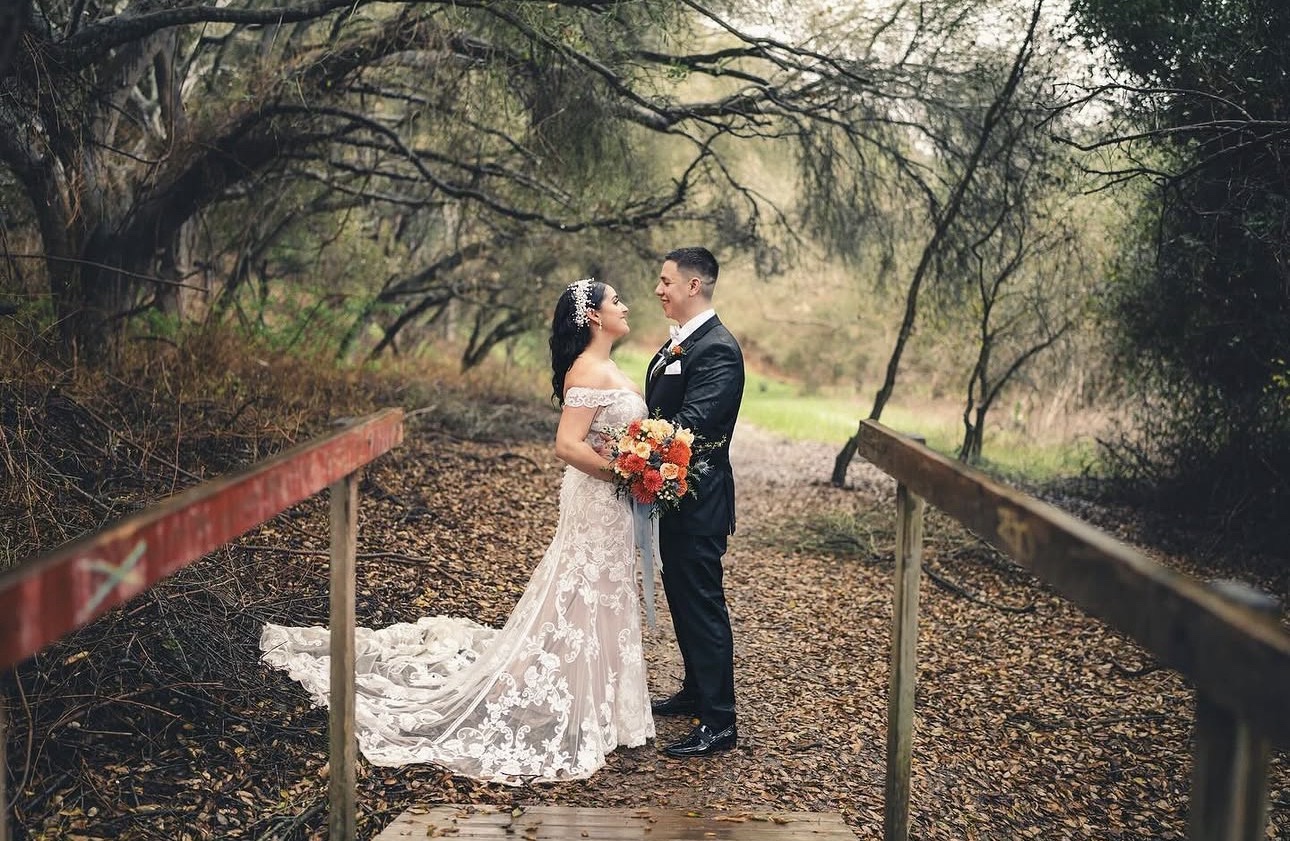 Anthony and Elizabeth on their wedding day, standing close together on a wooden bridge in the woods